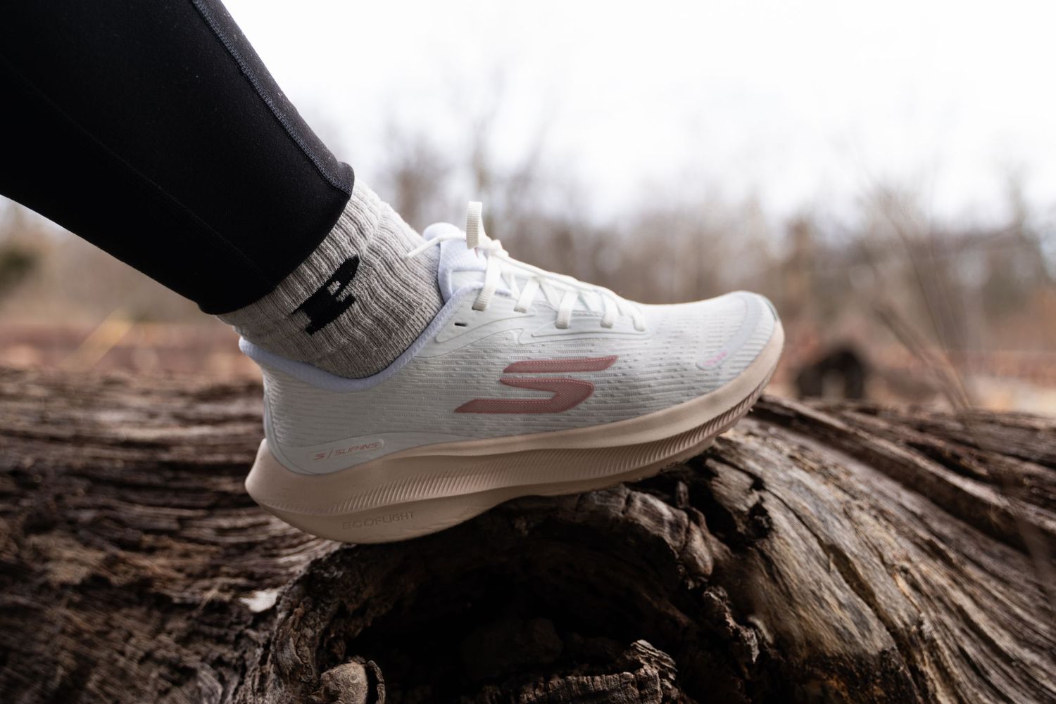 White sneakers balanced on a weathered wooden log in a natural outdoor setting.