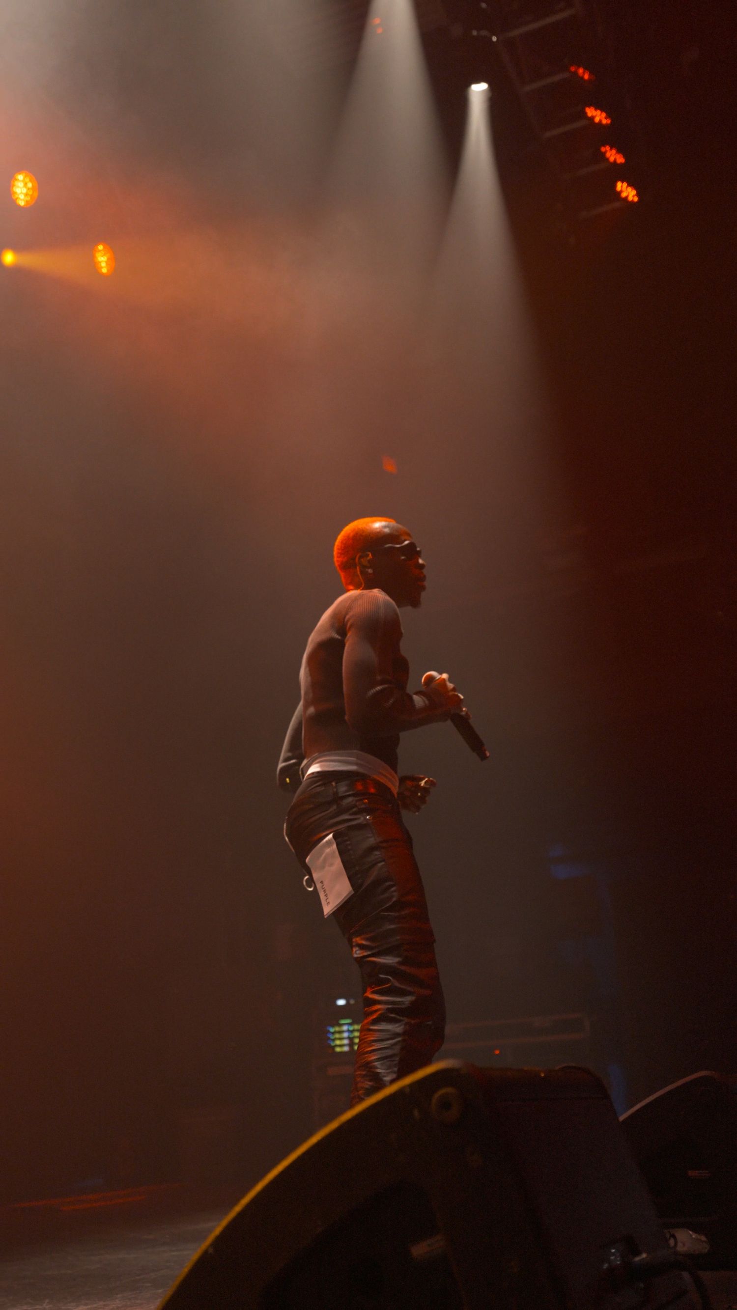 Performer silhouetted on stage with dramatic orange lighting and fog effects.
