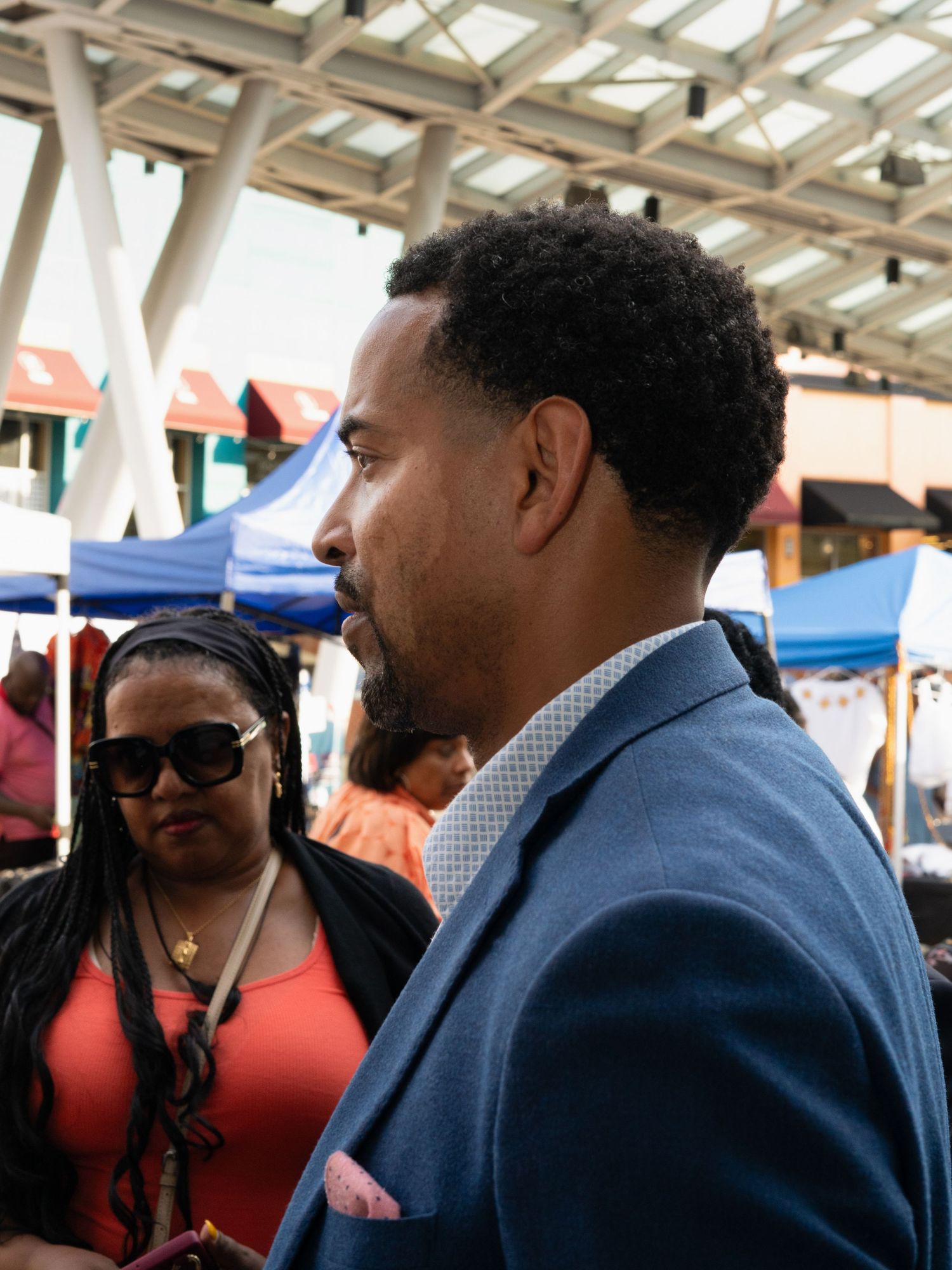 Group of people engaged in conversation under a covered outdoor marketplace.