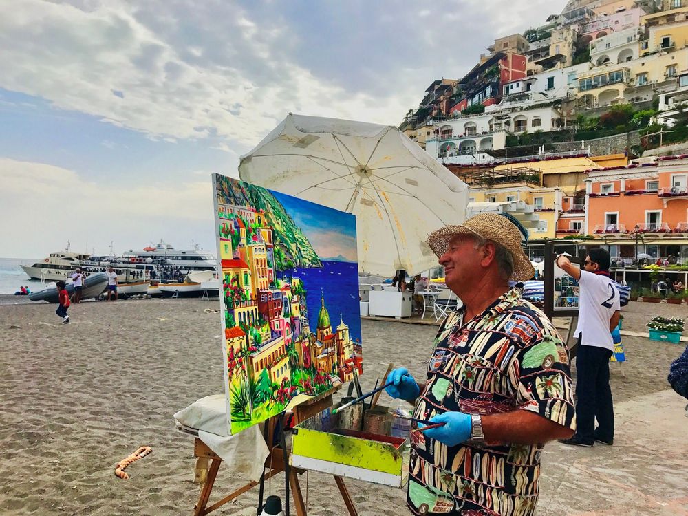 Artist painting colorful Positano coastal village on canvas at beachside easel, Amalfi Coast, Italy.