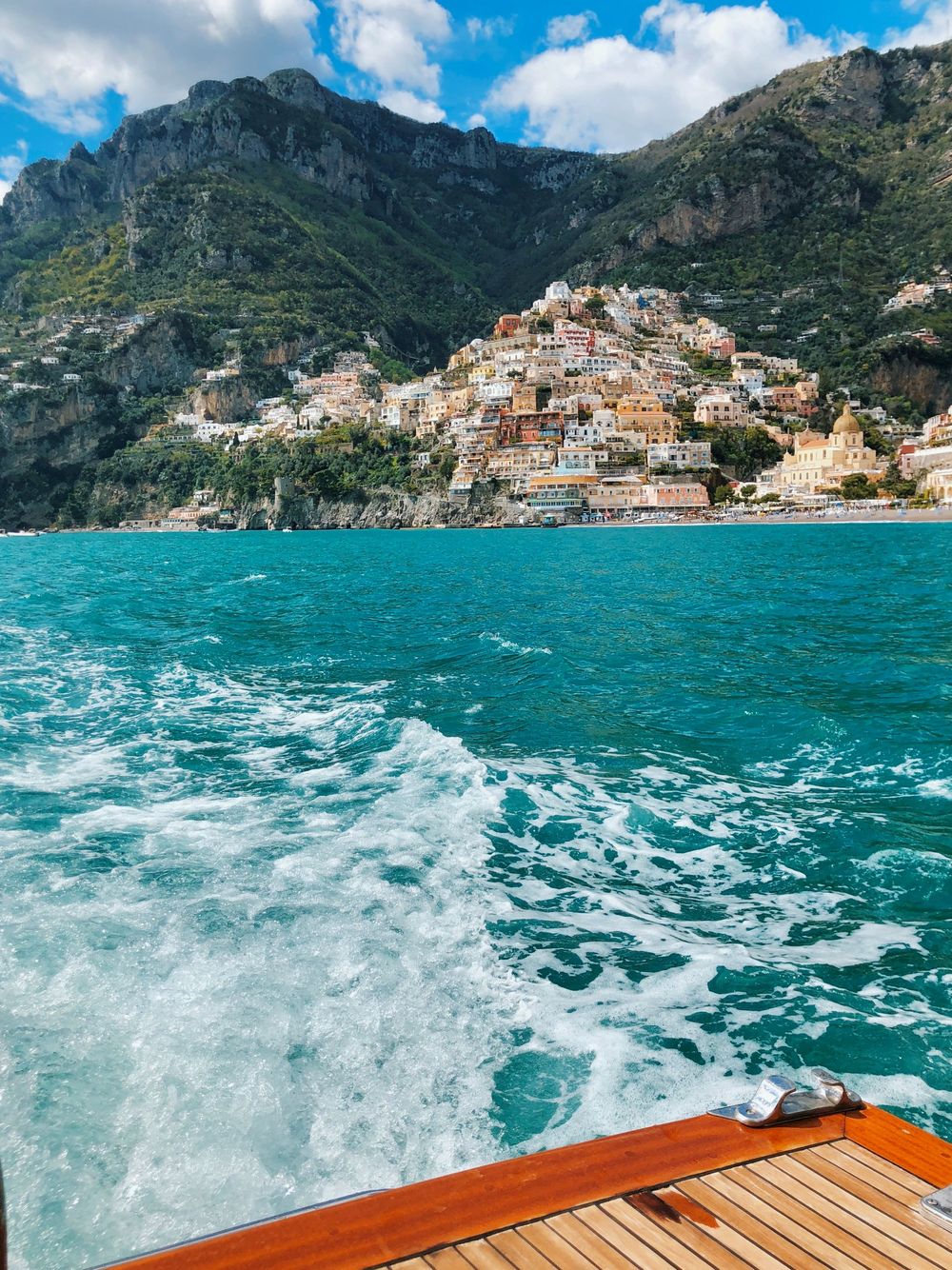 View from a wooden boat deck of turquoise waters and colorful Positano village on Amalfi Coast cliffs, Italy.