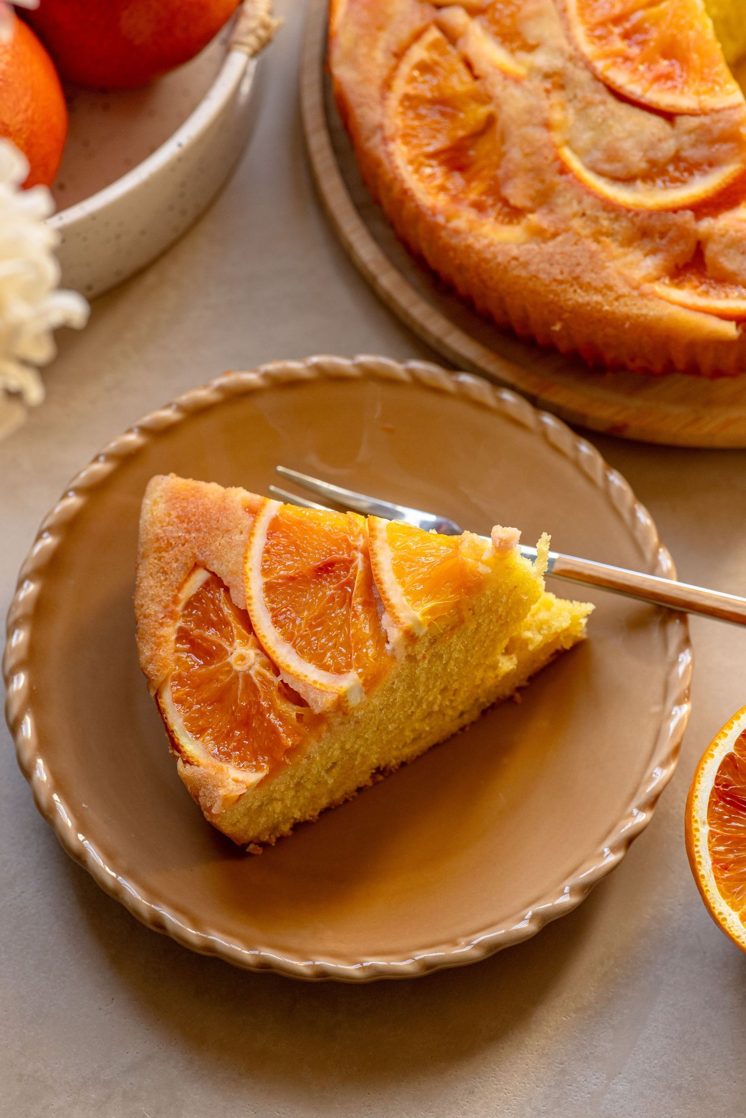 A slice of orange upside-down cake on a beige plate with a fork, showcasing caramelized orange slices on top.