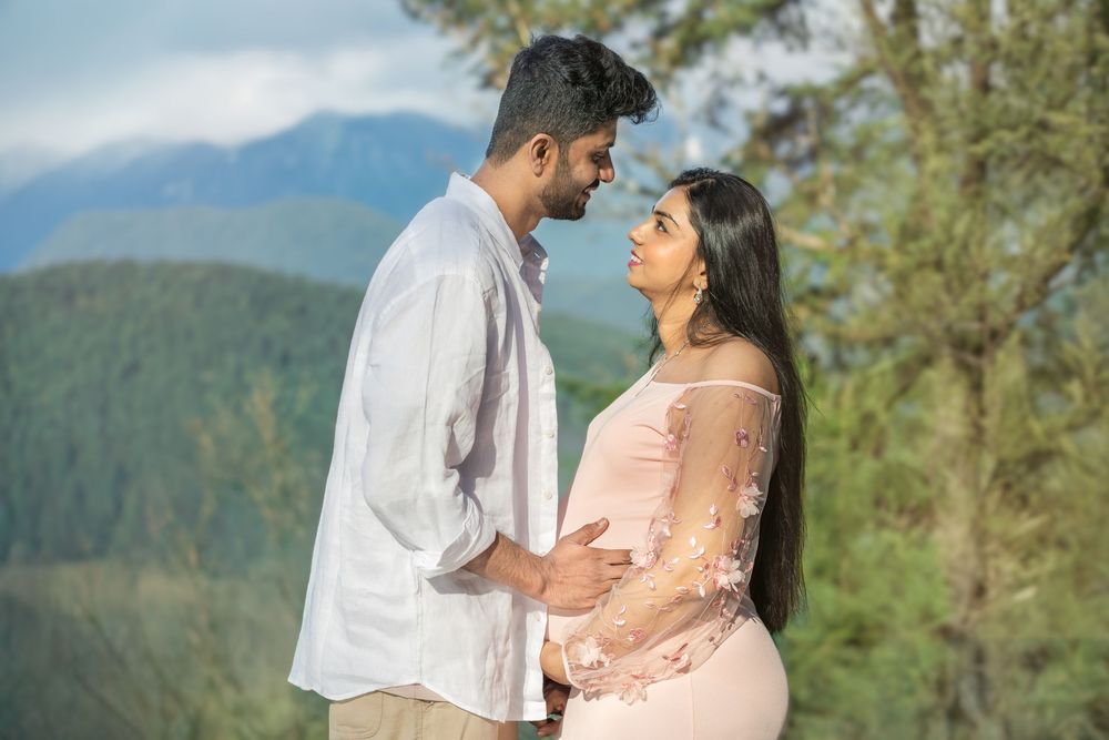 Couple sharing a tender moment outdoors with mountains and green trees in the background during a maternity photoshoot.