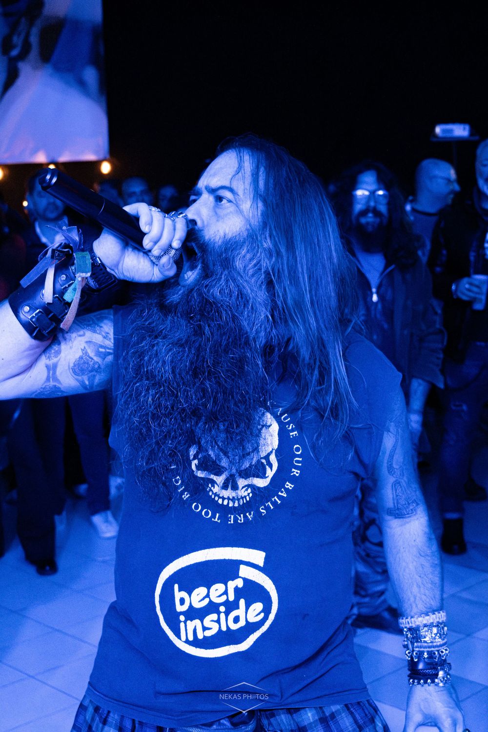 Man with long hair drinking from bottle wearing beer inside t-shirt at night event.