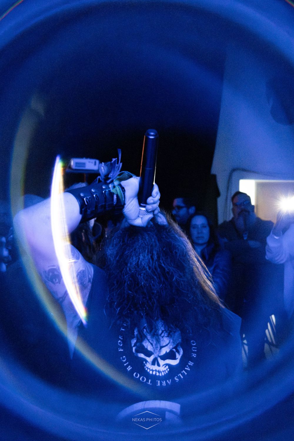 Performer holds microphone stand overhead with long hair flying at an intense live metal concert show.