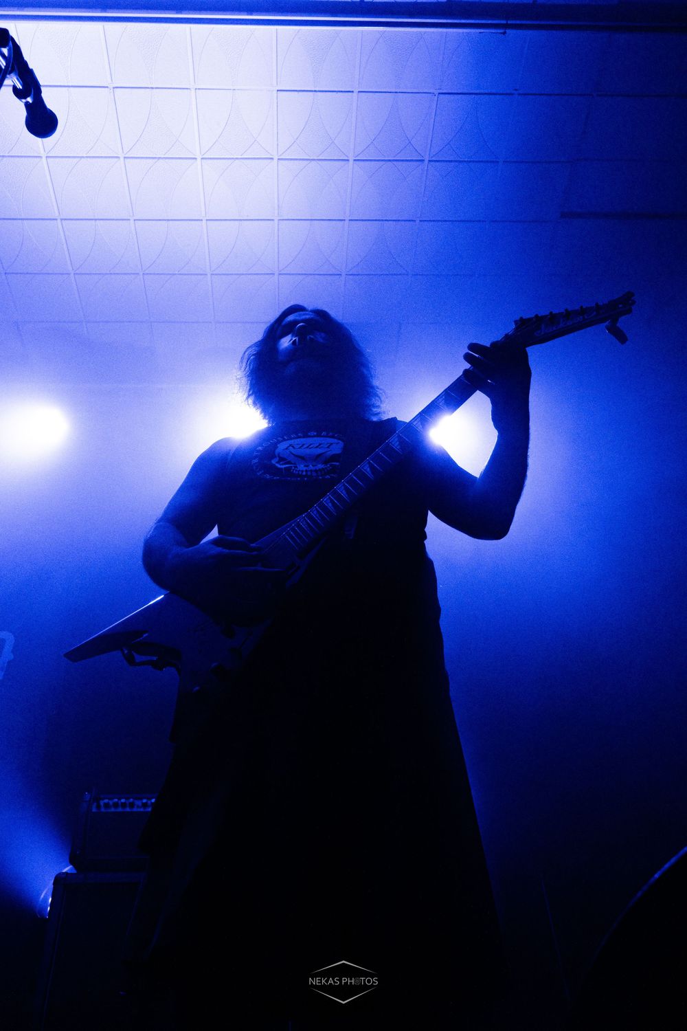 Silhouetted guitarist performing on stage bathed in dramatic blue light at a live metal concert.