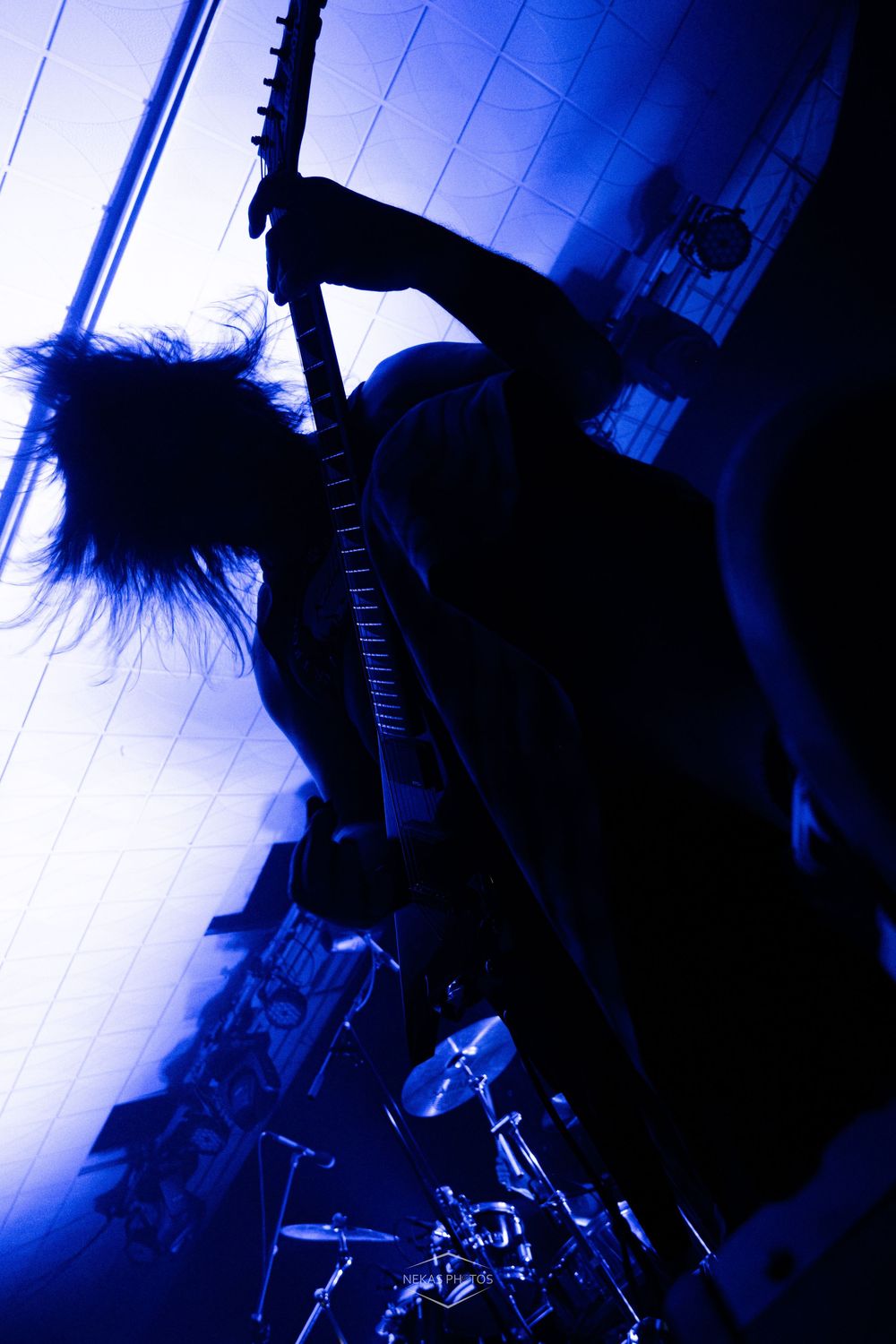 Silhouetted rock guitarist performing on stage under dramatic blue lighting with drum kit visible in background.