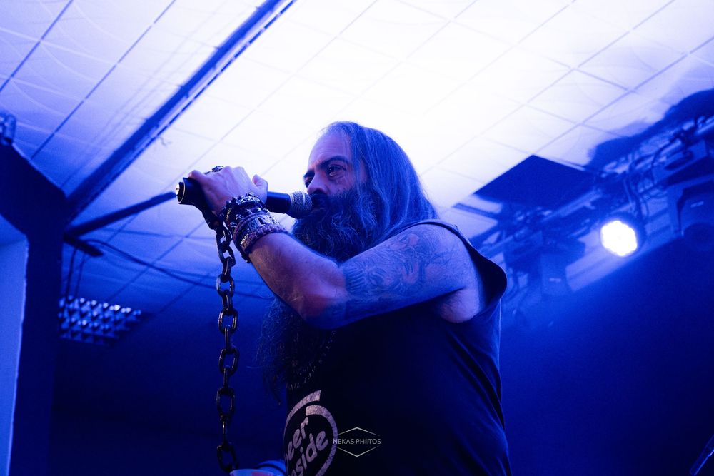 Heavy metal vocalist performing on stage under blue lights, holding a chain while singing into a microphone.