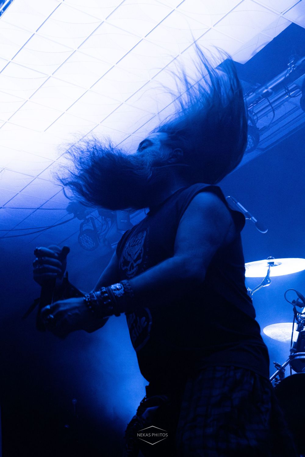 Metal musician headbanging on stage under dramatic blue lighting with hair flying, performing live concert.