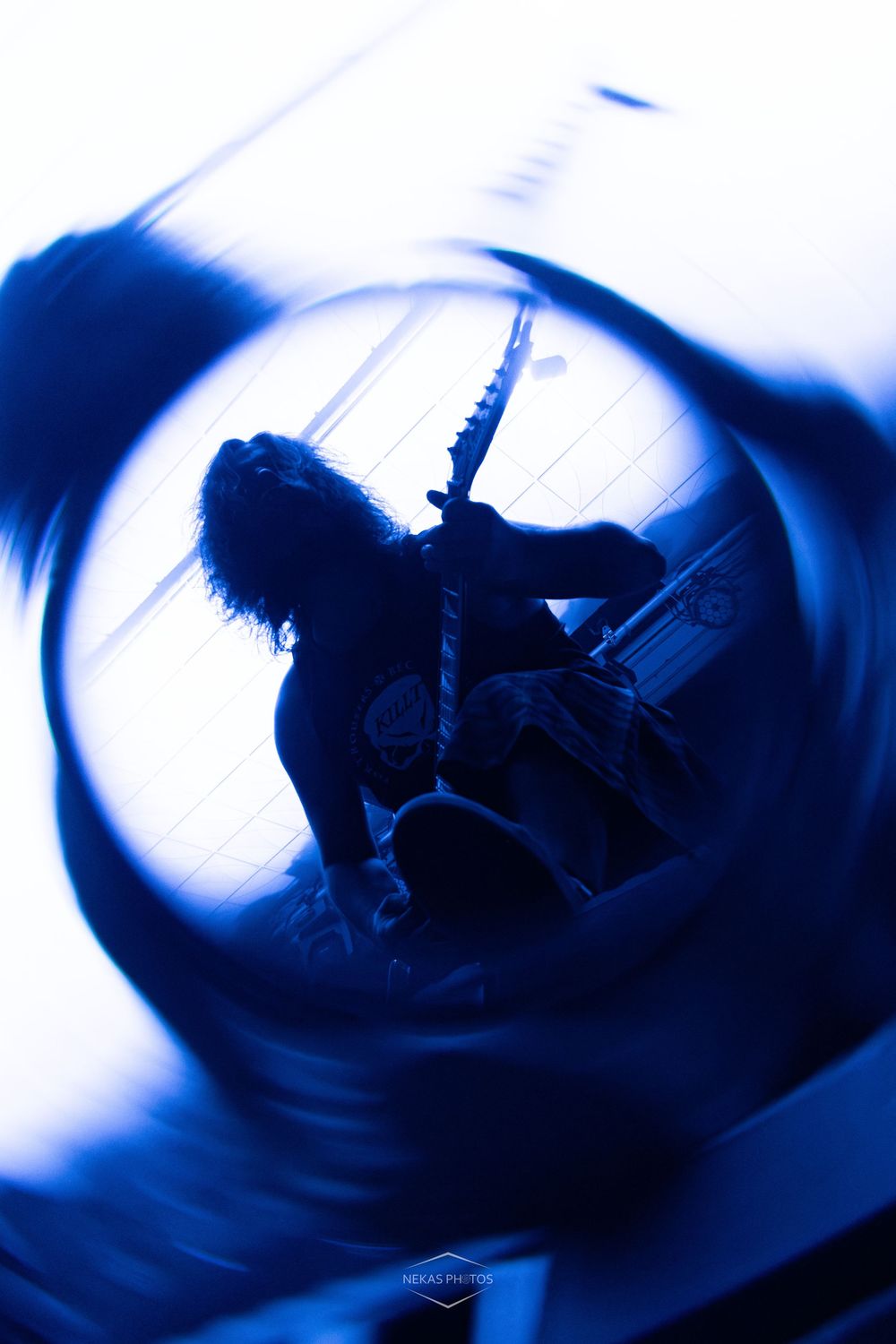 Blue-tinted silhouette of a guitarist performing on stage with dramatic circular motion blur effect.