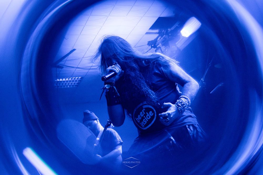 Heavy metal performer singing on stage under dramatic blue lighting with fisheye lens effect.