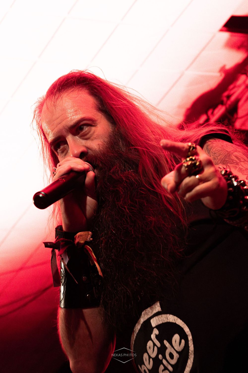 Heavy metal vocalist with long red hair and beard performing on stage under dramatic red lighting.