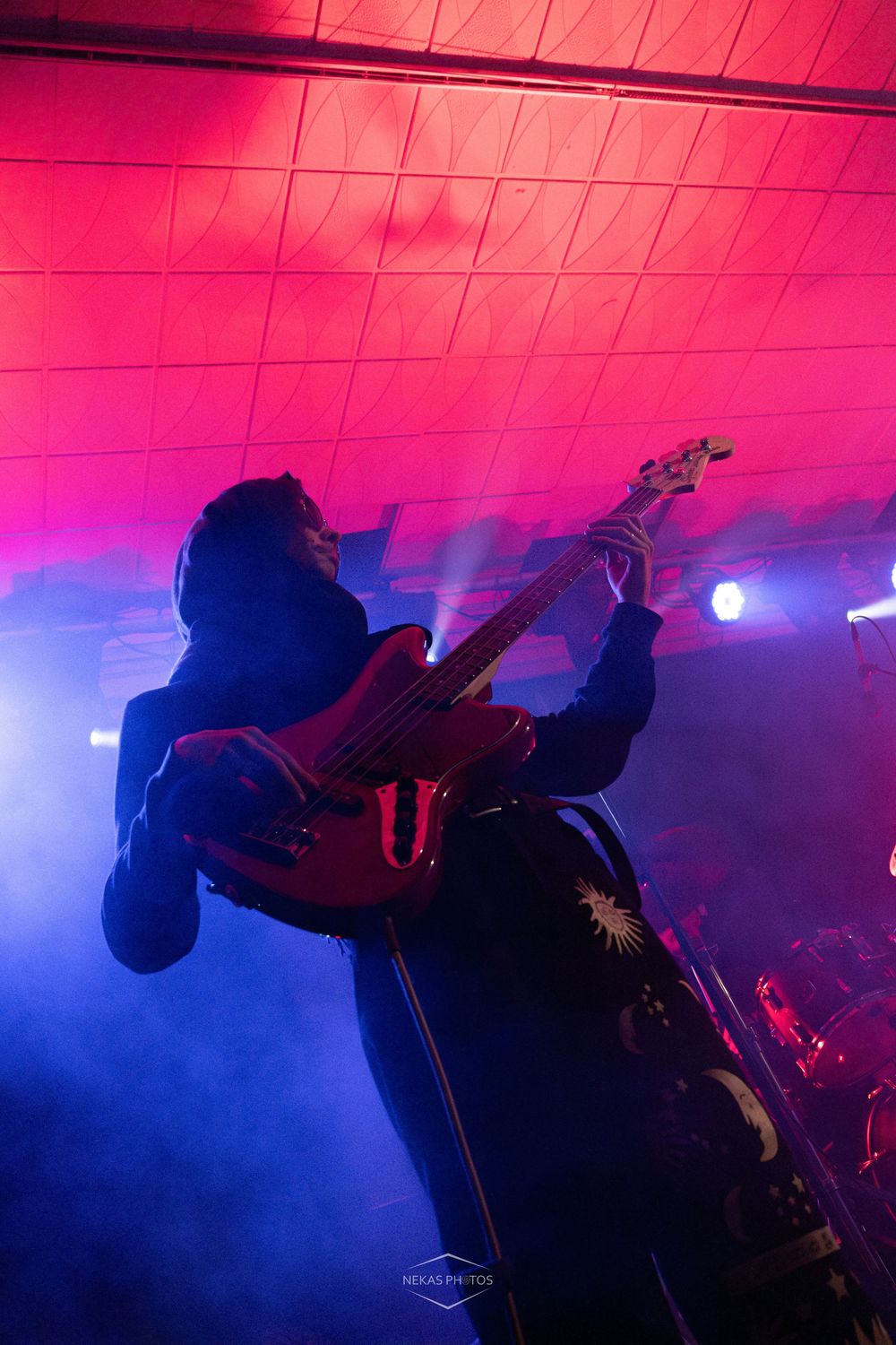 Guitarist performing on stage under red and blue lights with smoke effects at a live concert.