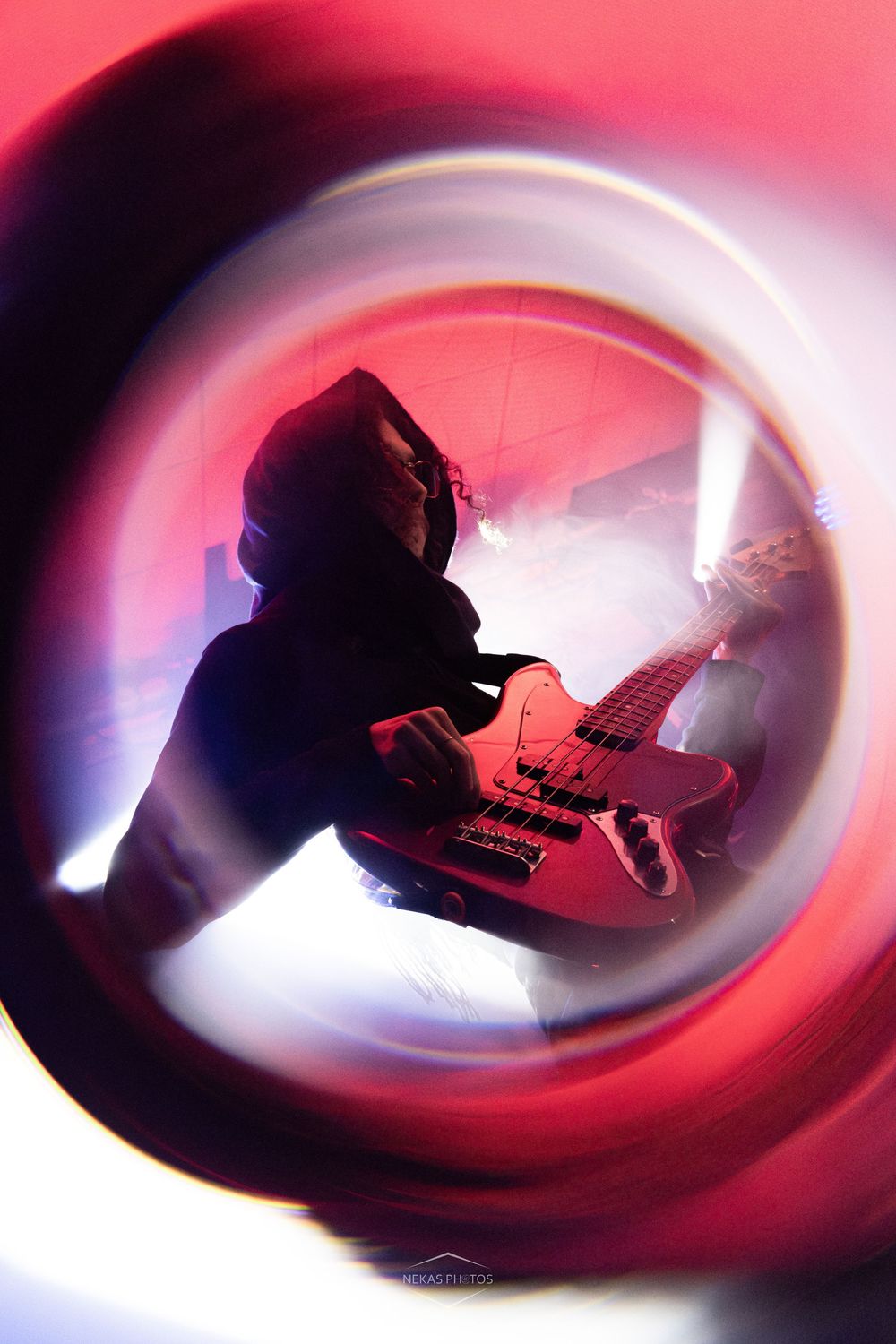 Creative fisheye lens shot of a hooded guitarist performing on a red-lit smoky concert stage.