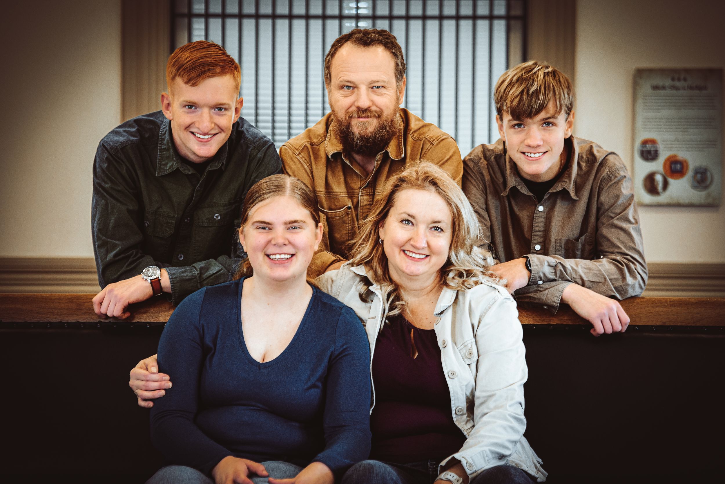 A cheerful family of five posing together indoors, with three adults standing behind two smiling women seated in front.