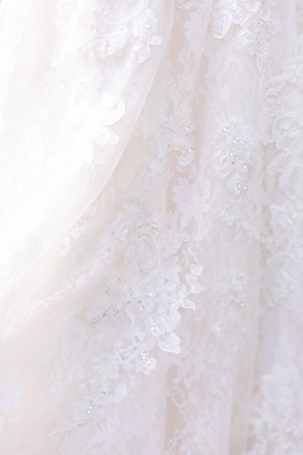 Close-up detail of intricate floral lace and beading on white wedding dress fabric.