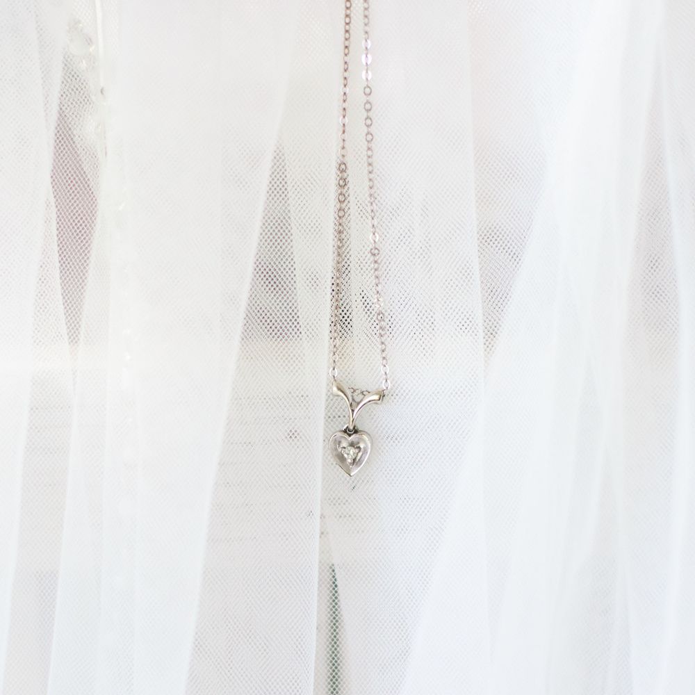 Delicate heart-shaped diamond pendant necklace hanging against a white bridal veil.