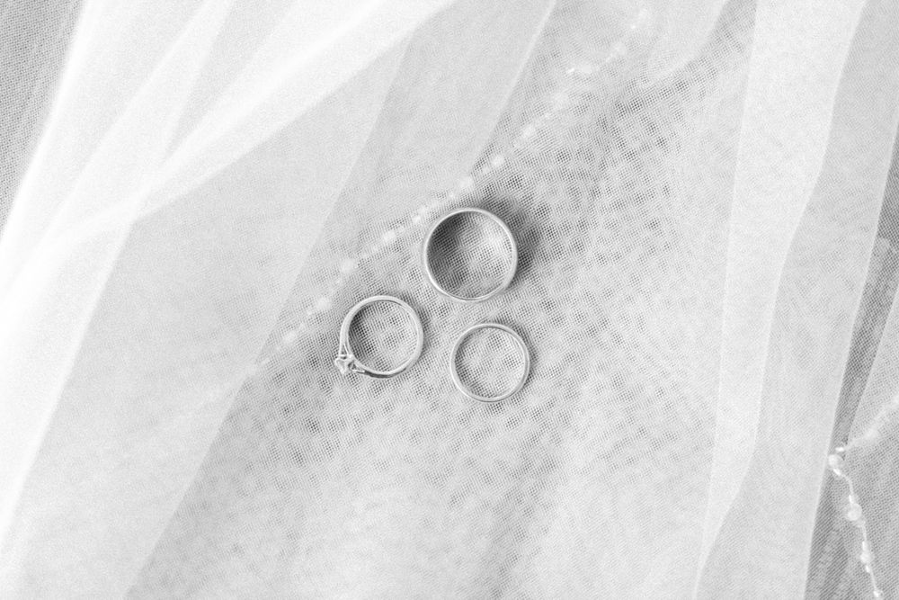 Three silver wedding bands arranged on white bridal veil fabric in black and white photo.