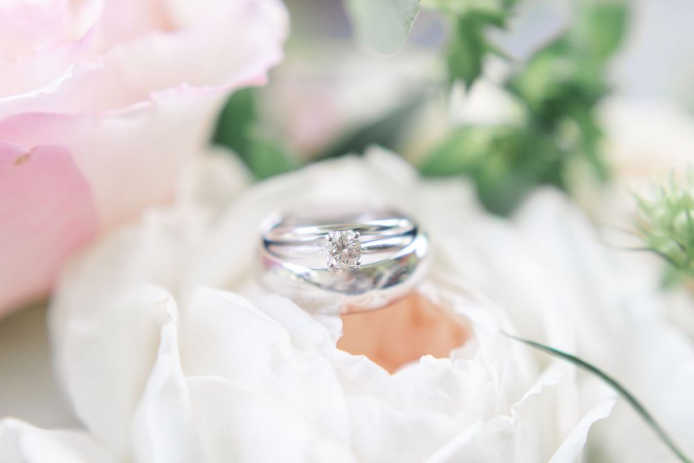 Diamond engagement ring and silver wedding bands resting inside a white rose bloom.
