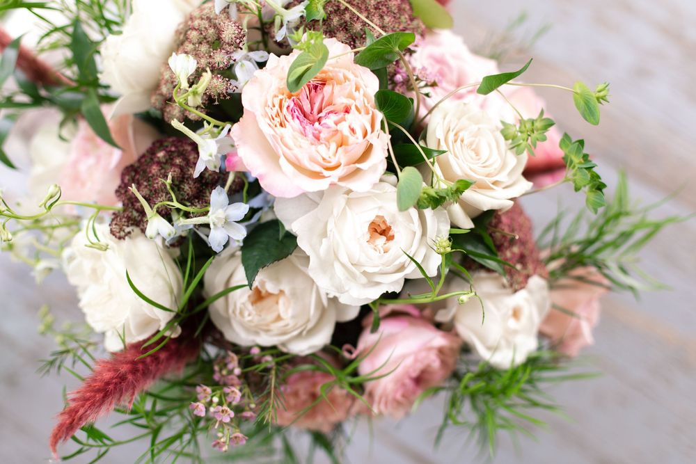 Romantic bridal bouquet with blush pink and cream roses, wildflowers, and greenery.