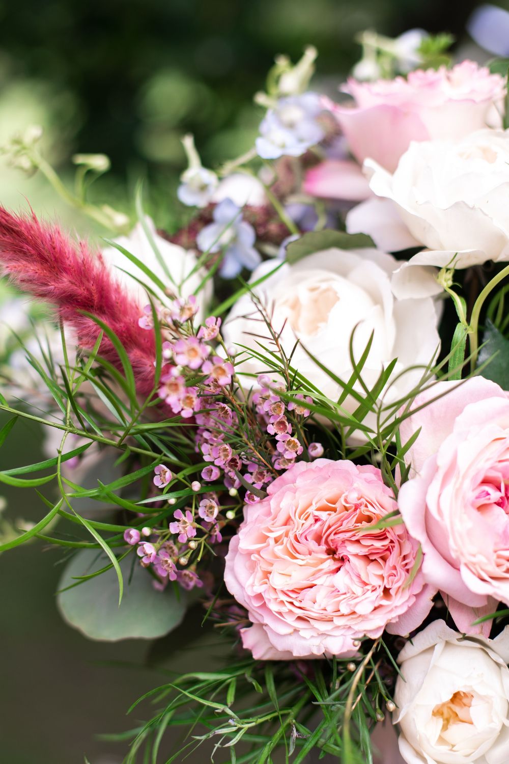 Elegant wedding bouquet featuring pink roses, white peonies, blue flowers, and greenery with pink pampas grass accents.