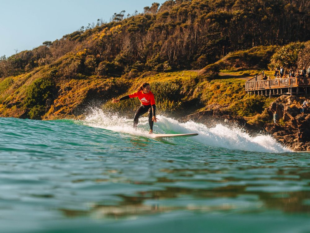 Woman with a competition jersey smiling during a turn on a longboard at a surfing competition at Scotts Head, NSW Loggerheads