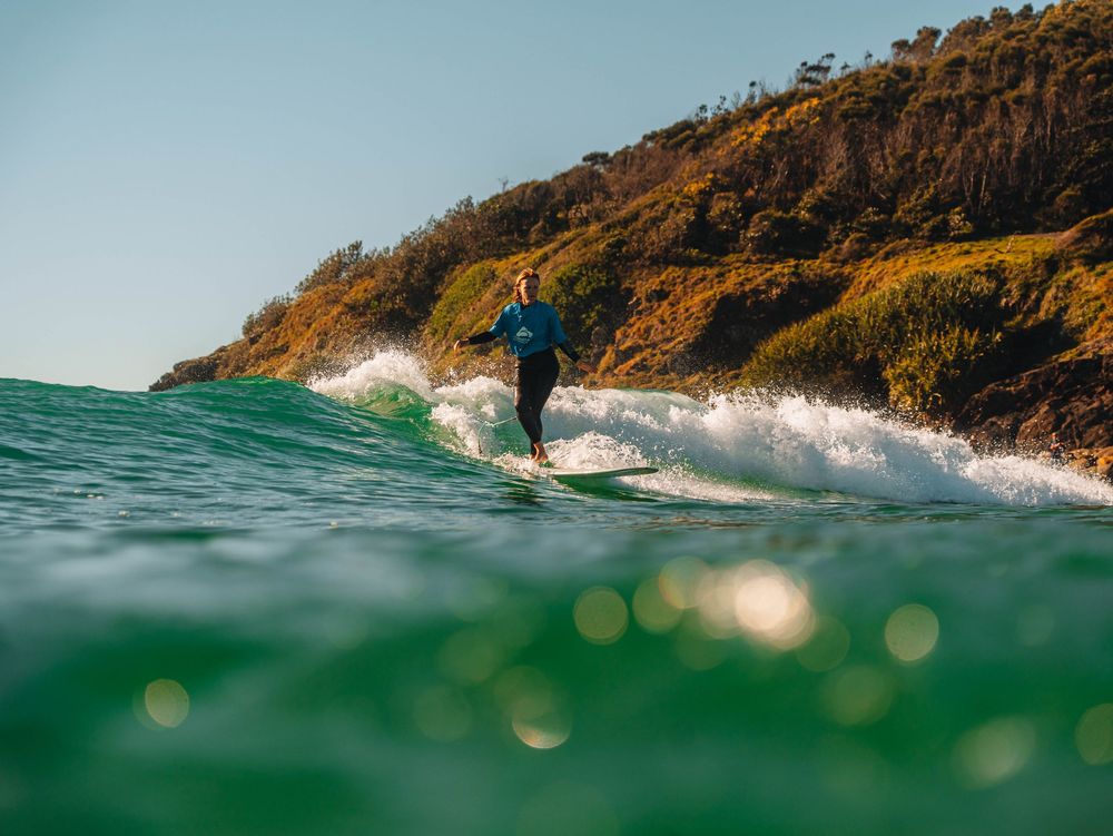 Woman with cross stepping over a longboard at a surfing competition at Scotts Head, NSW Loggerheads with ocean sparkle in foreground