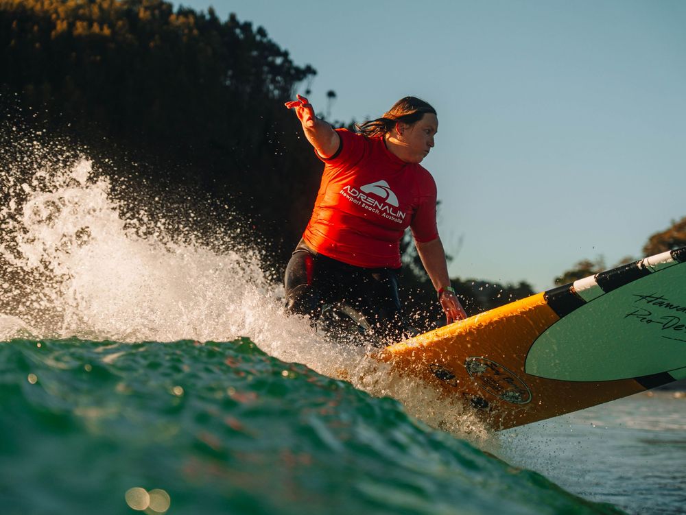 Woman with a competition jersey throwing a big top turn on a wave with a longboard at a surfing competition at Scotts Head, NSW Loggerheads