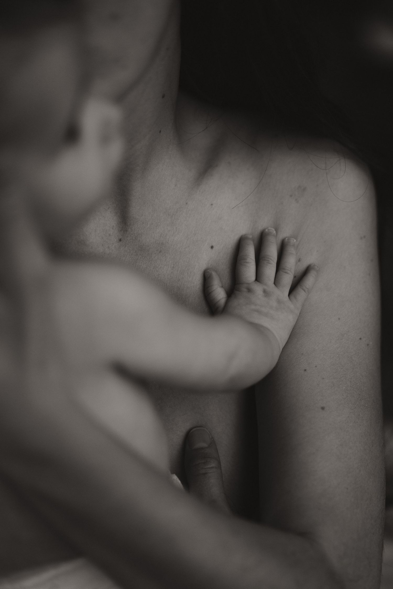 Black and white photo of a newborn baby's tiny hand resting gently on a parent's chest.