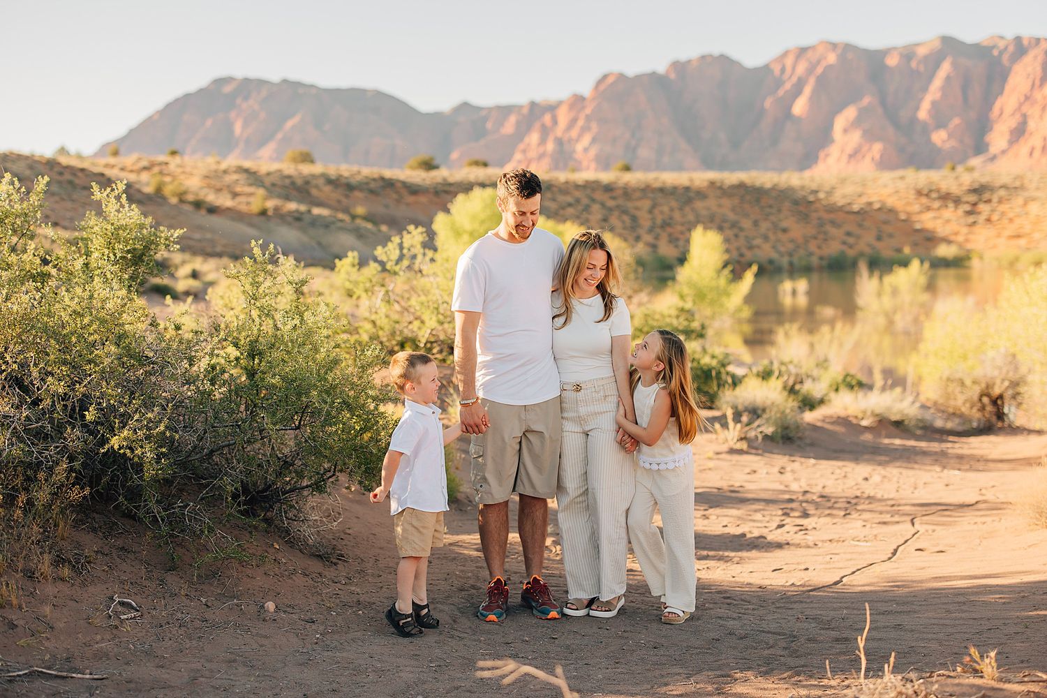 Family of four posing on a desert trail with mountains and golden hour light in the background.