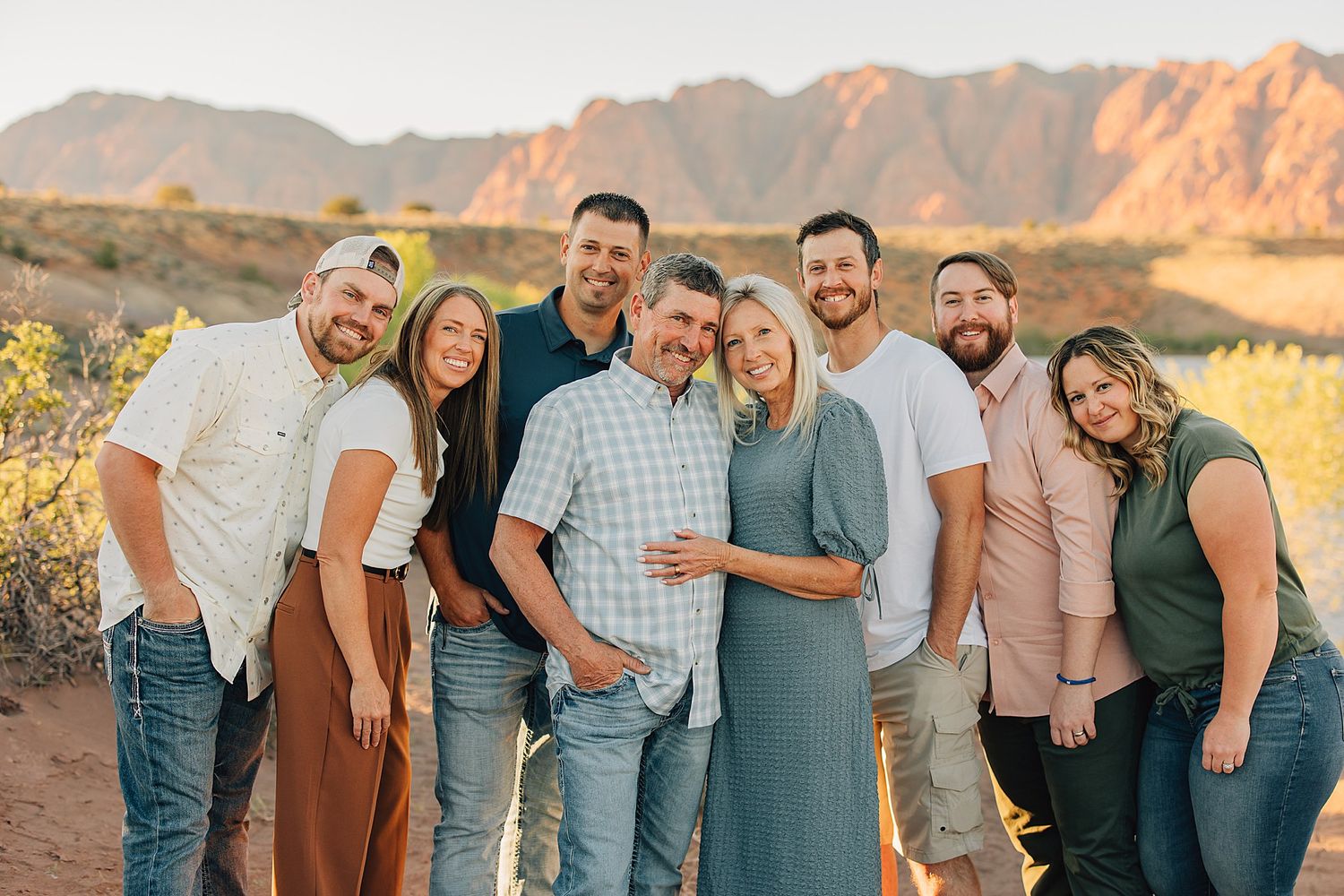A large family poses together smiling in a desert landscape with red rock mountains at golden hour.