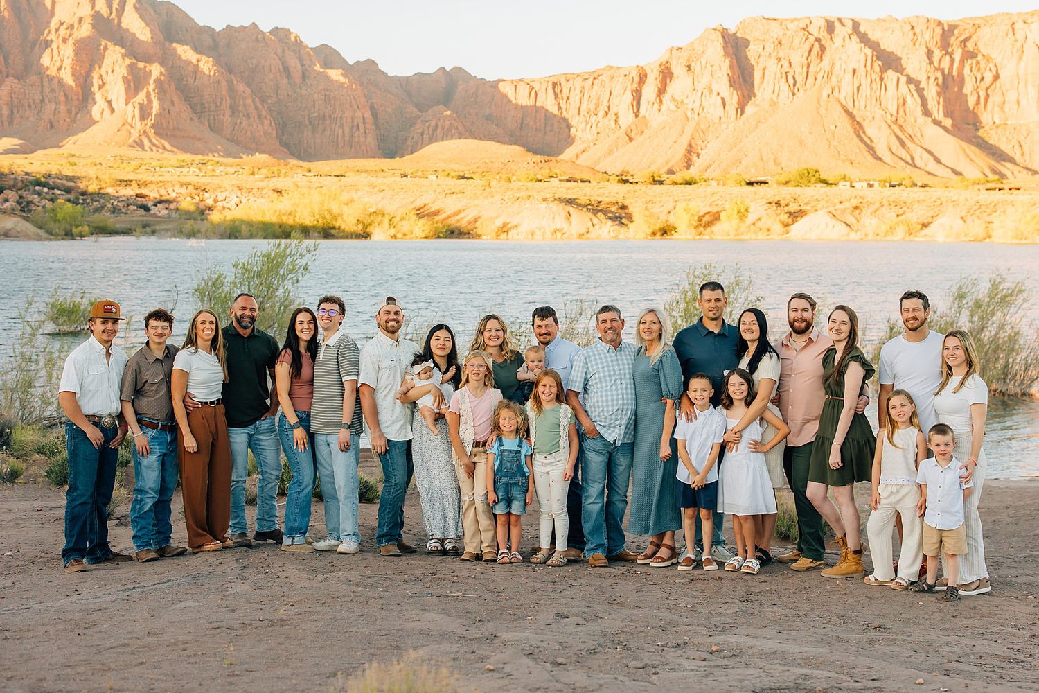 Large family group photo outdoors near a river with red rock canyon backdrop in warm golden light.