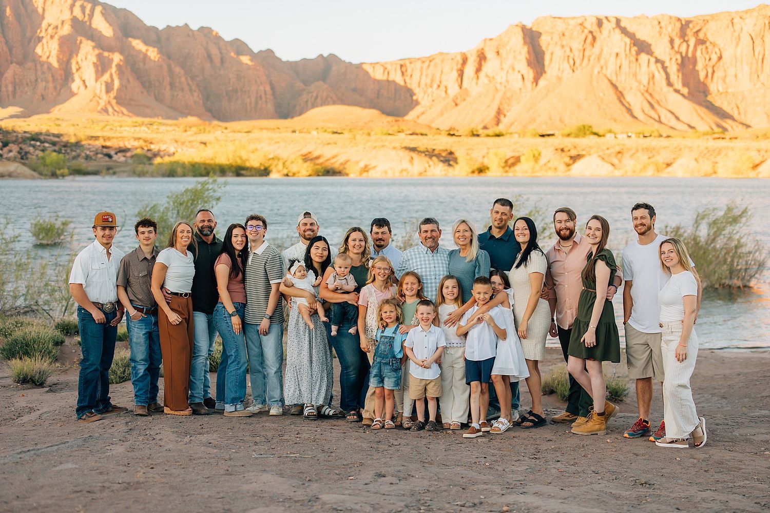 Large family group portrait outdoors near a river with red rock canyon cliffs at golden hour sunset.