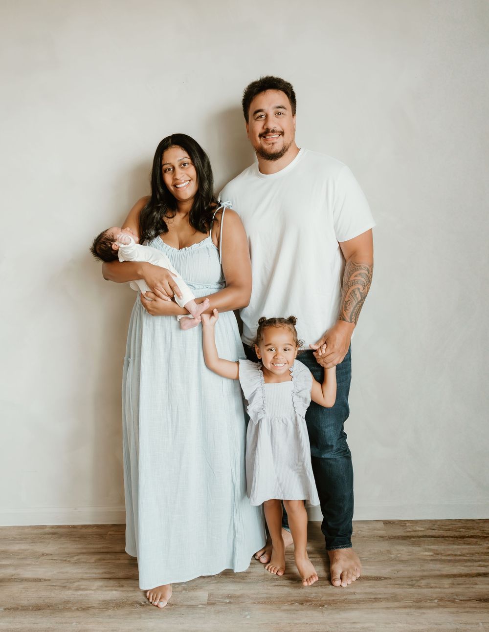 Happy family of four posing for a newborn portrait, parents with toddler daughter and baby in a bright studio.