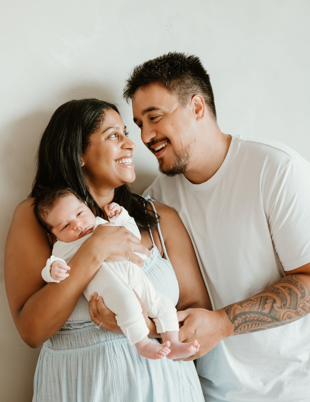 Happy couple smiling at each other while holding their newborn baby against a white background.