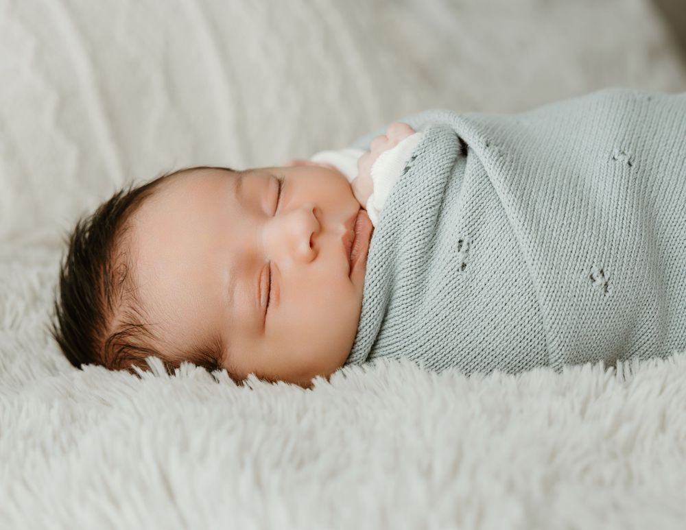 Peaceful newborn baby swaddled in a soft blue knit blanket, sleeping on a fluffy white surface.
