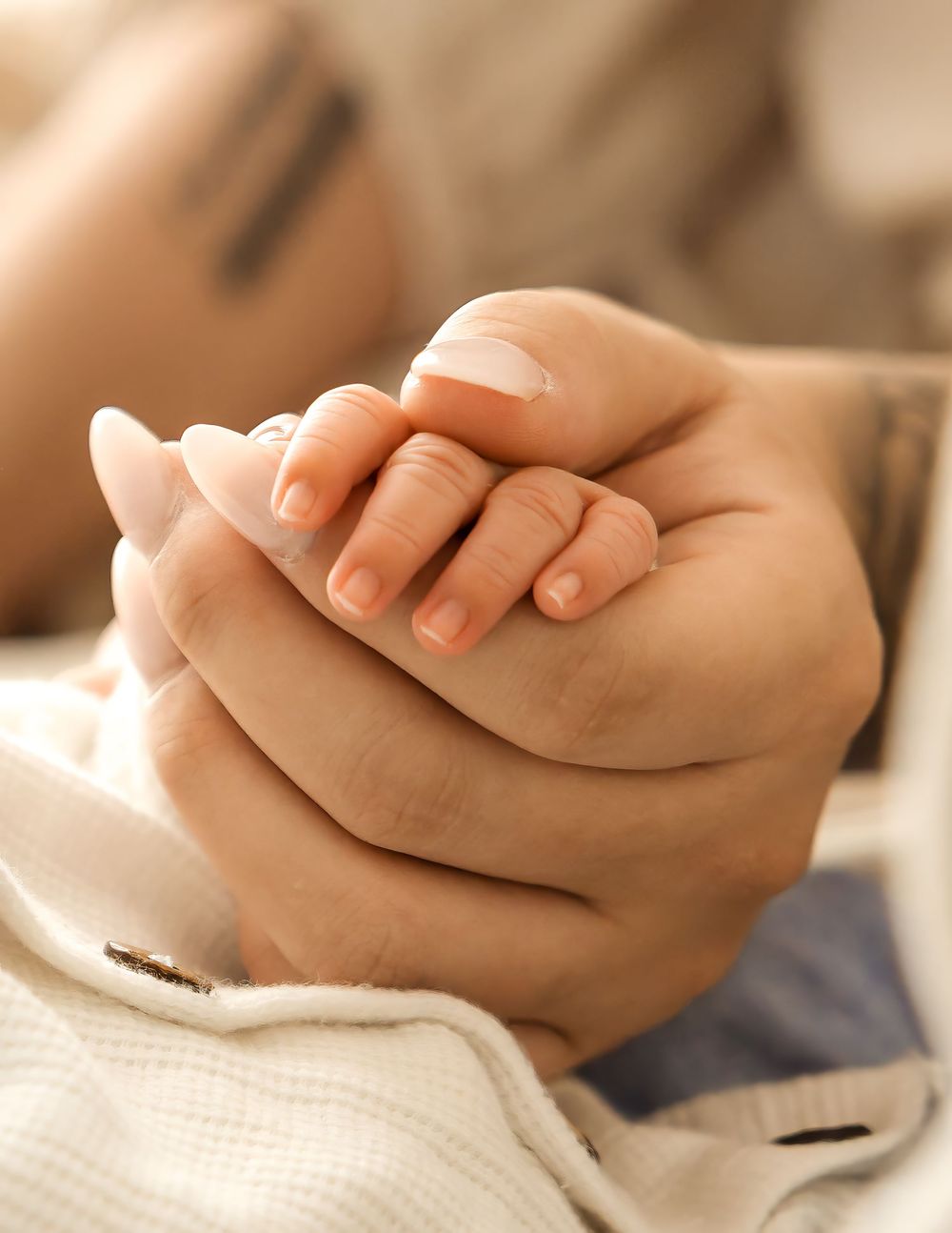 Adult hands gently cradling a newborn baby's tiny hand, symbolizing love and parental care.