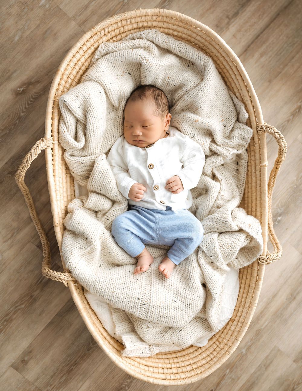 Peaceful newborn baby sleeping in a woven Moses basket with a soft knit blanket.