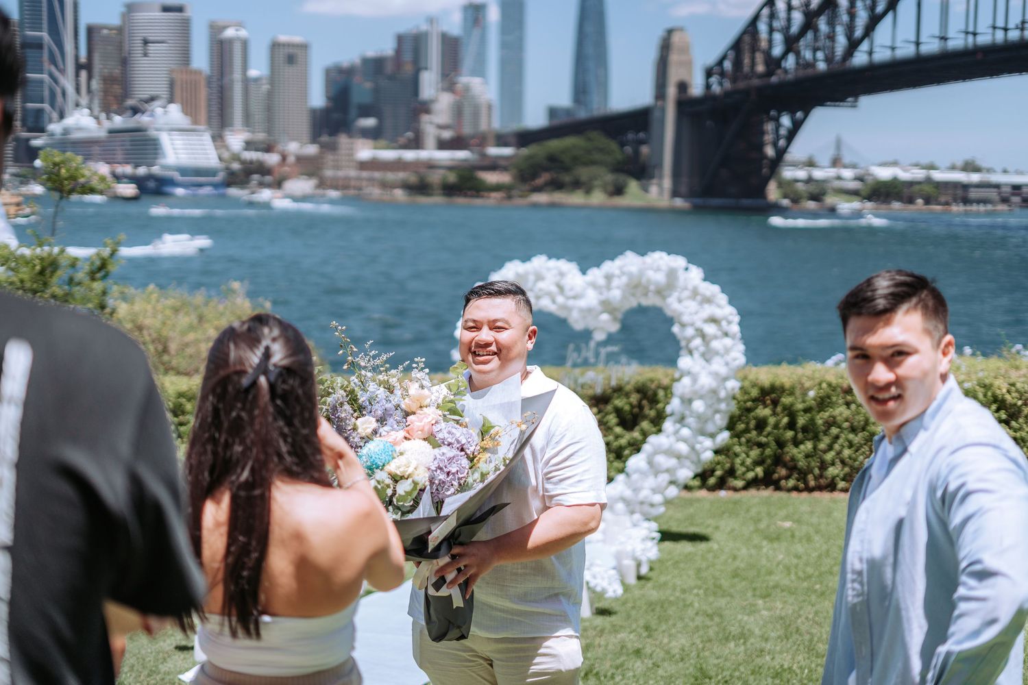 Outdoor wedding ceremony with heart balloon arch near Sydney Harbour Bridge waterfront.