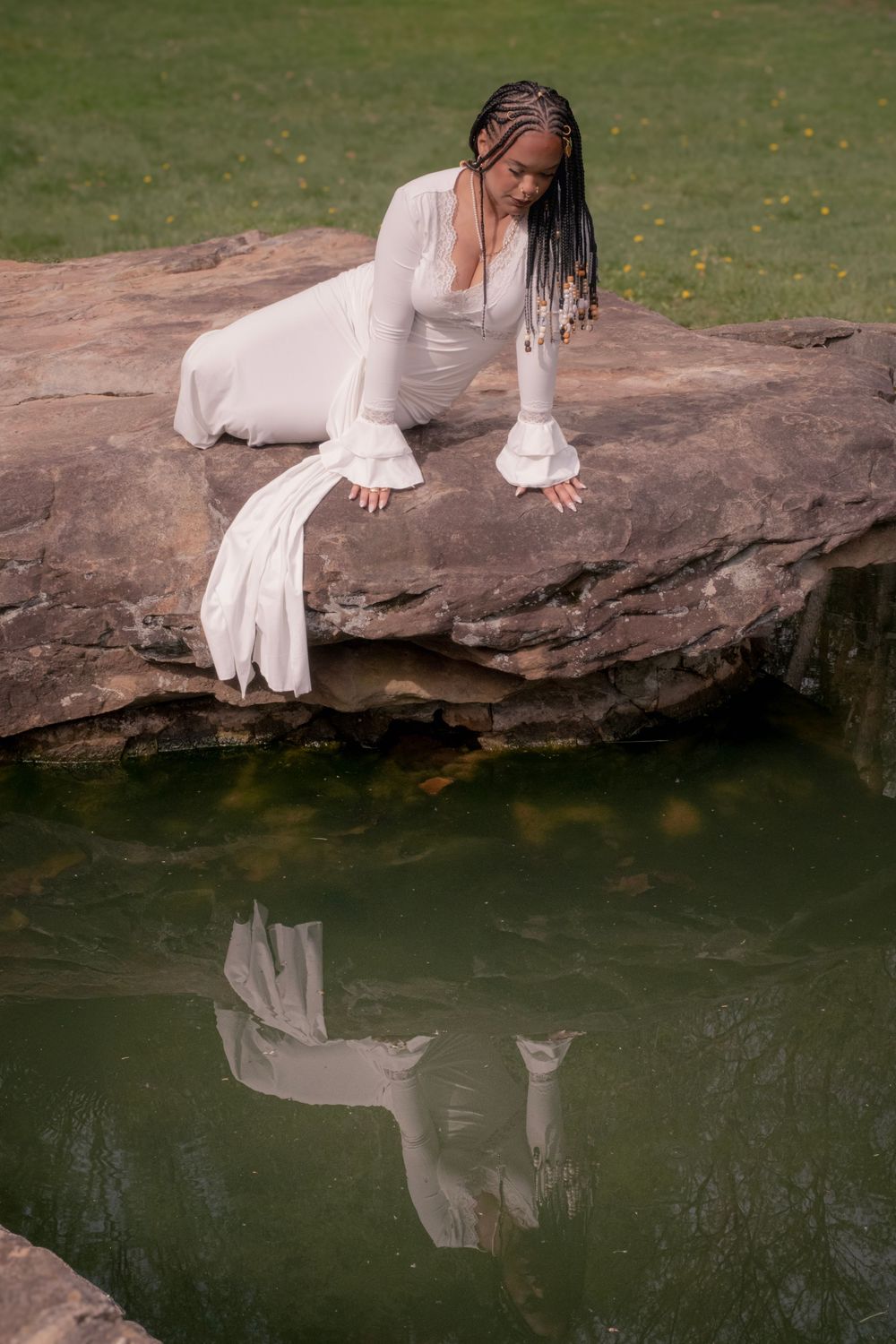 Woman in white dress kneeling on rocks by a reflective pond, her mirror image visible in the still green water.
Uniontown, PA
