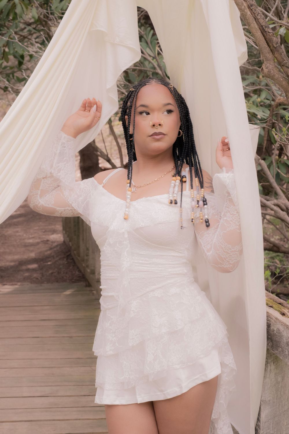 Young woman in white lace mini dress with braids poses gracefully between sheer white curtains on a wooden bridge.

Uniontown, PA