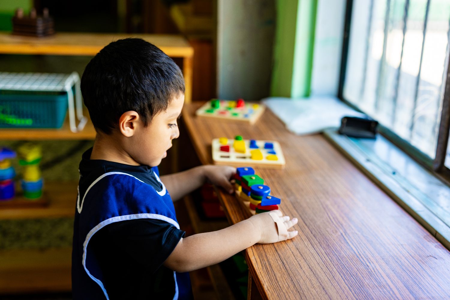 Young boy playing with colorful educational toys at a wooden table in a bright classroom setting.