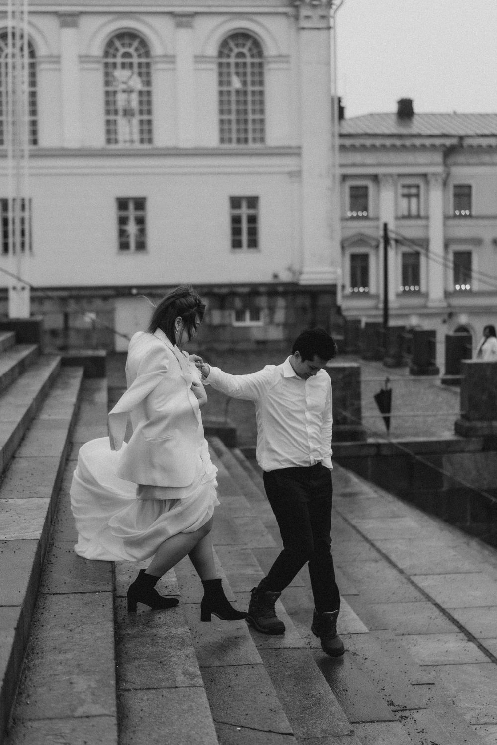 Black and white engagement photo of a couple running together near Helsinki Cathedral