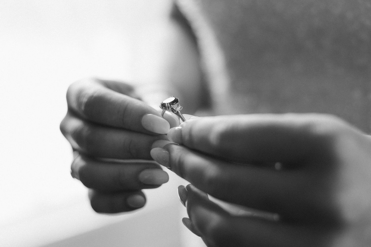 Black and white photo of hands holding a diamond engagement ring.