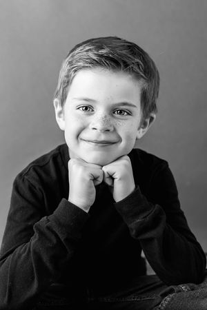 Moreno Valley kids photographer: Black and white portrait of a freckled boy resting his chin on his hands with a gentle smile.