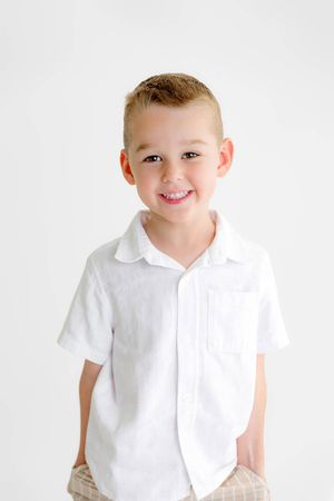 Smiling young boy in a white short-sleeve button-up shirt posing against a white background.