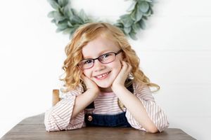 Portrait photographer in Murrieta: Smiling red-haired girl with glasses and curly hair.