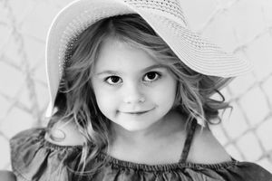 Black and white portrait of a pretty little girl wearing a wide brim sun hat.