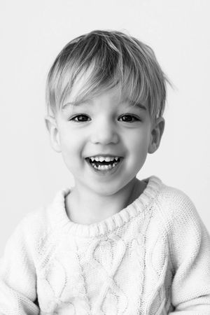 Black and white portrait of a laughing blonde toddler boy wearing a cable-knit sweater.