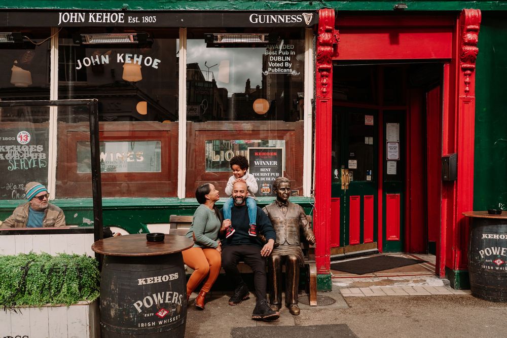 Friends laughing outside John Kehoe pub with Guinness signage in Dublin, Ireland.